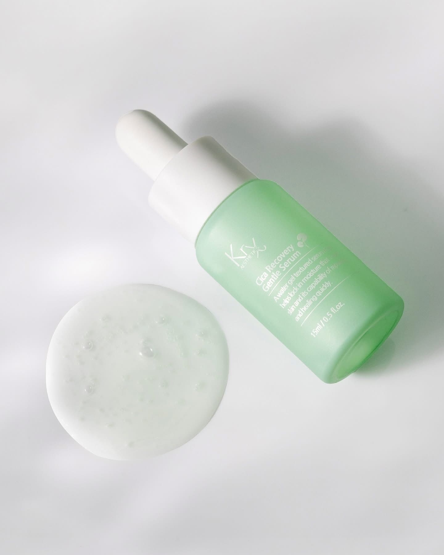 A light green serum bottle with a white dropper cap beside a small puddle of the translucent, gel-like product.