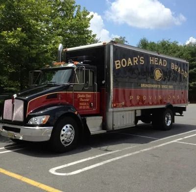 Boar's Head Brand refrigerated truck, parked in a lot, with red and black cab and black container.