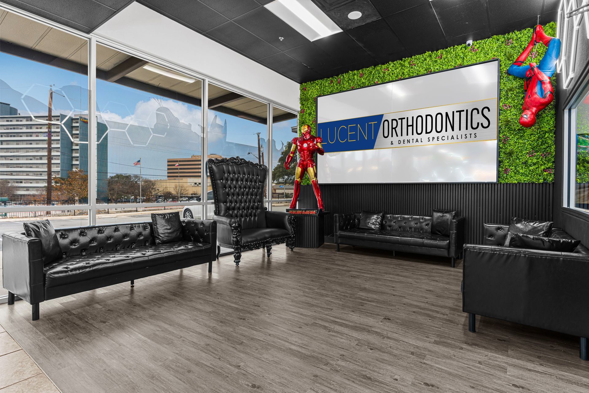 Lucent Orthodontics, San Antonio. A modern waiting room featuring black leather furniture, an Iron Man statue, and a Spiderman figure on a green wall.