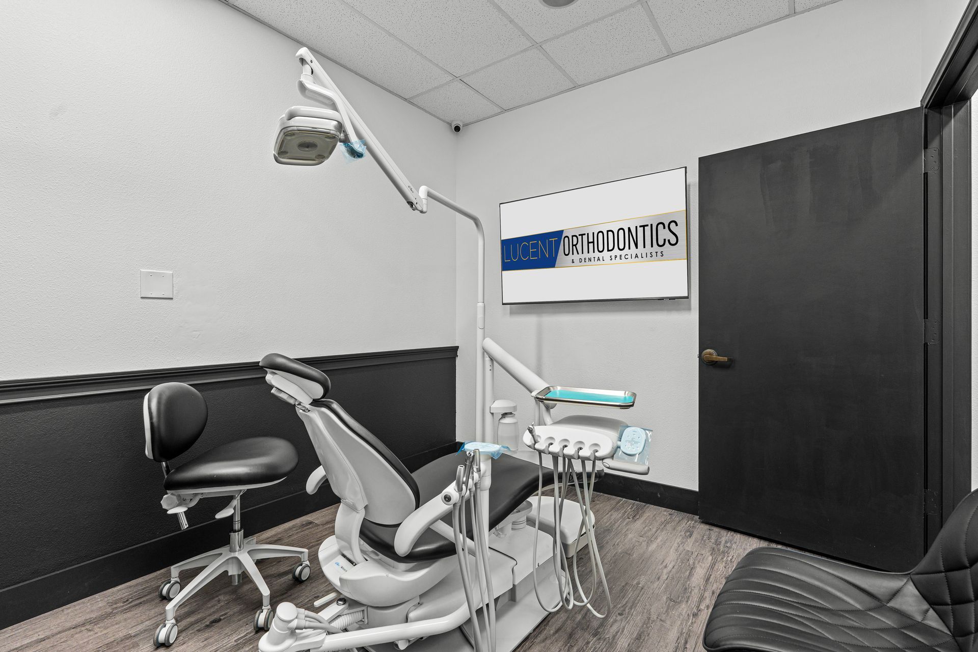 Lucent Orthodontics, San Antonio. A modern orthodontist's exam room featuring a dental chair, equipment, and a wall-mounted sign in a clean, neutral space.
