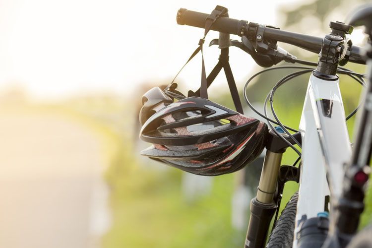 A bicycle helmet hanging from the handle of a white bike in the countryside.