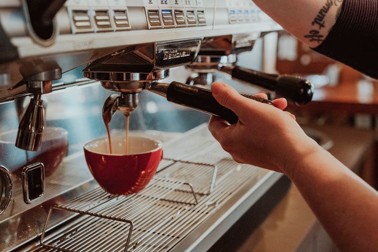 A person is pouring coffee into a red cup from a coffee machine.
