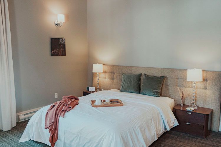 A bedroom with a bed , nightstand , lamps and a tray on the bed.