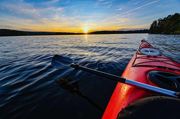 Kayak rouge sur l'eau au coucher du soleil; pagaie à la main, soleil à l'horizon, cadre calme.