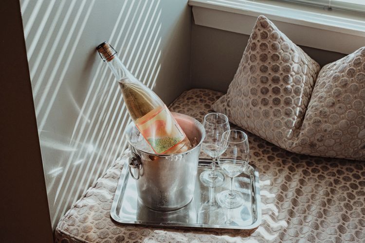 Une bouteille de mousseux est dans un seau sur un plateau à côté de verres à vin posé sur une banquette.