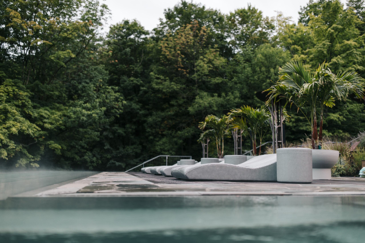 Modern outdoor pool with mist, stone loungers, and lush green trees in the background