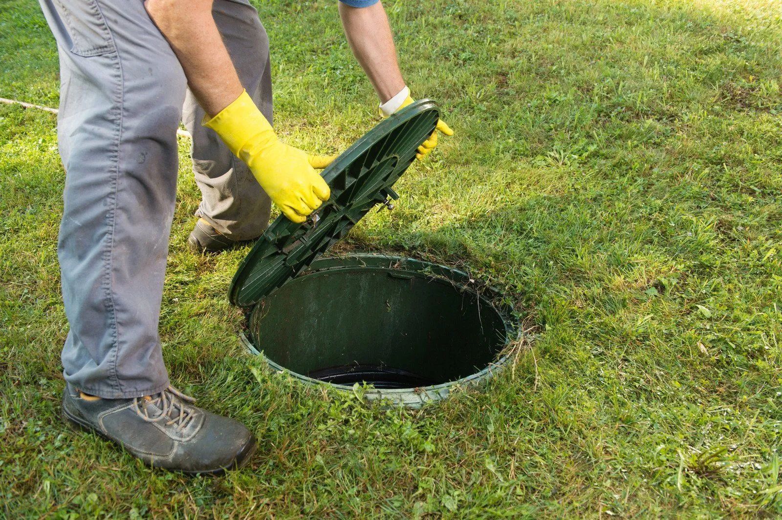 Worker in yellow gloves opening a green manhole cover on grass