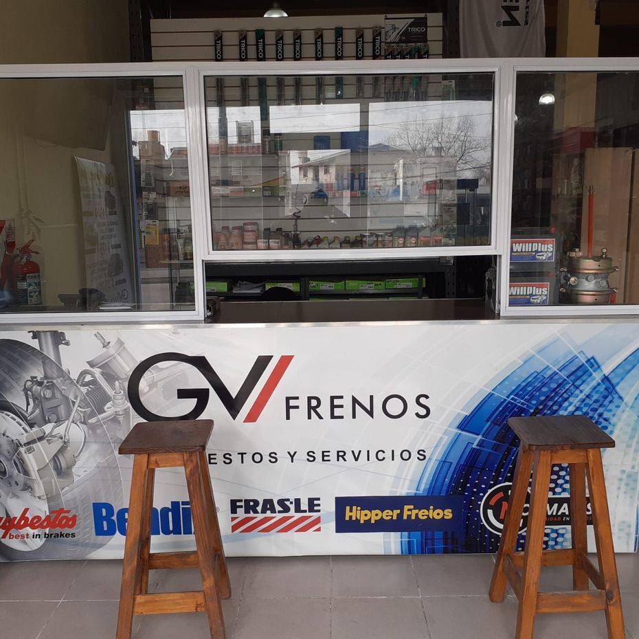 Mostrador de taller mecánico pequeño con un cartel de Gv Frenos y dos taburetes de madera delante.