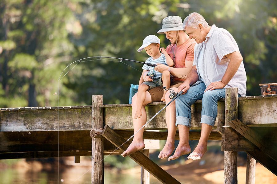 A family fishing from a wooden dock: a father, grandfather, and child watch a fishing rod bend over water.