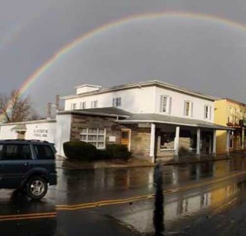 Double rainbow over a two-story white building, wet street with parked car.