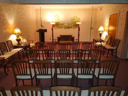 Interior of a funeral home chapel with rows of chairs facing a podium and altar, softly lit.