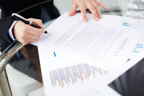 Person signing a contract at a table with charts and a glass of water.