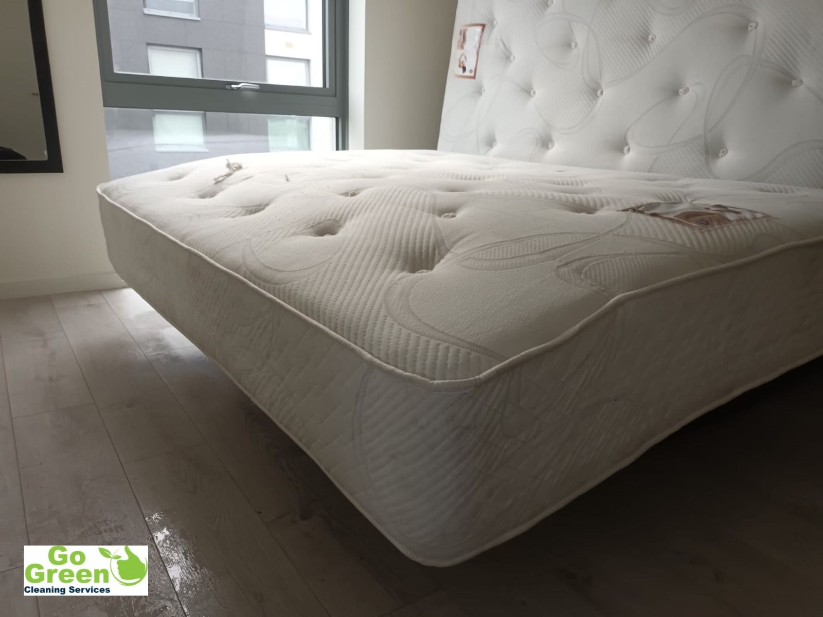 White mattress with tufted headboard in a room with a window and wood floor.