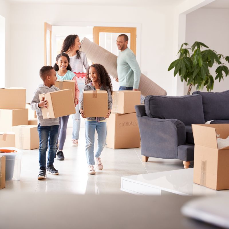 Family moving into a new home, carrying boxes and a rug.