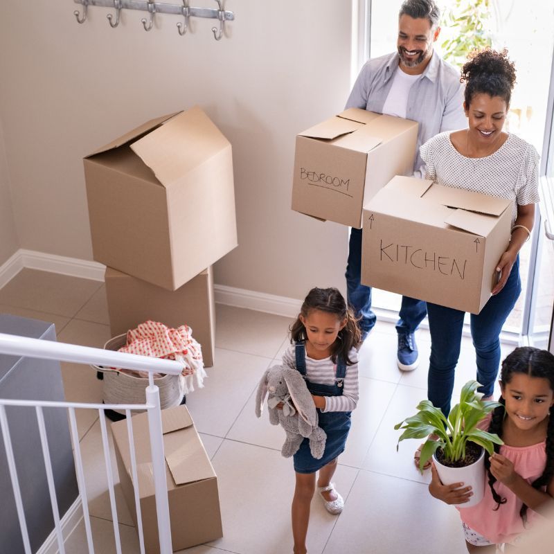 Family moving into a new home, carrying boxes and belongings.