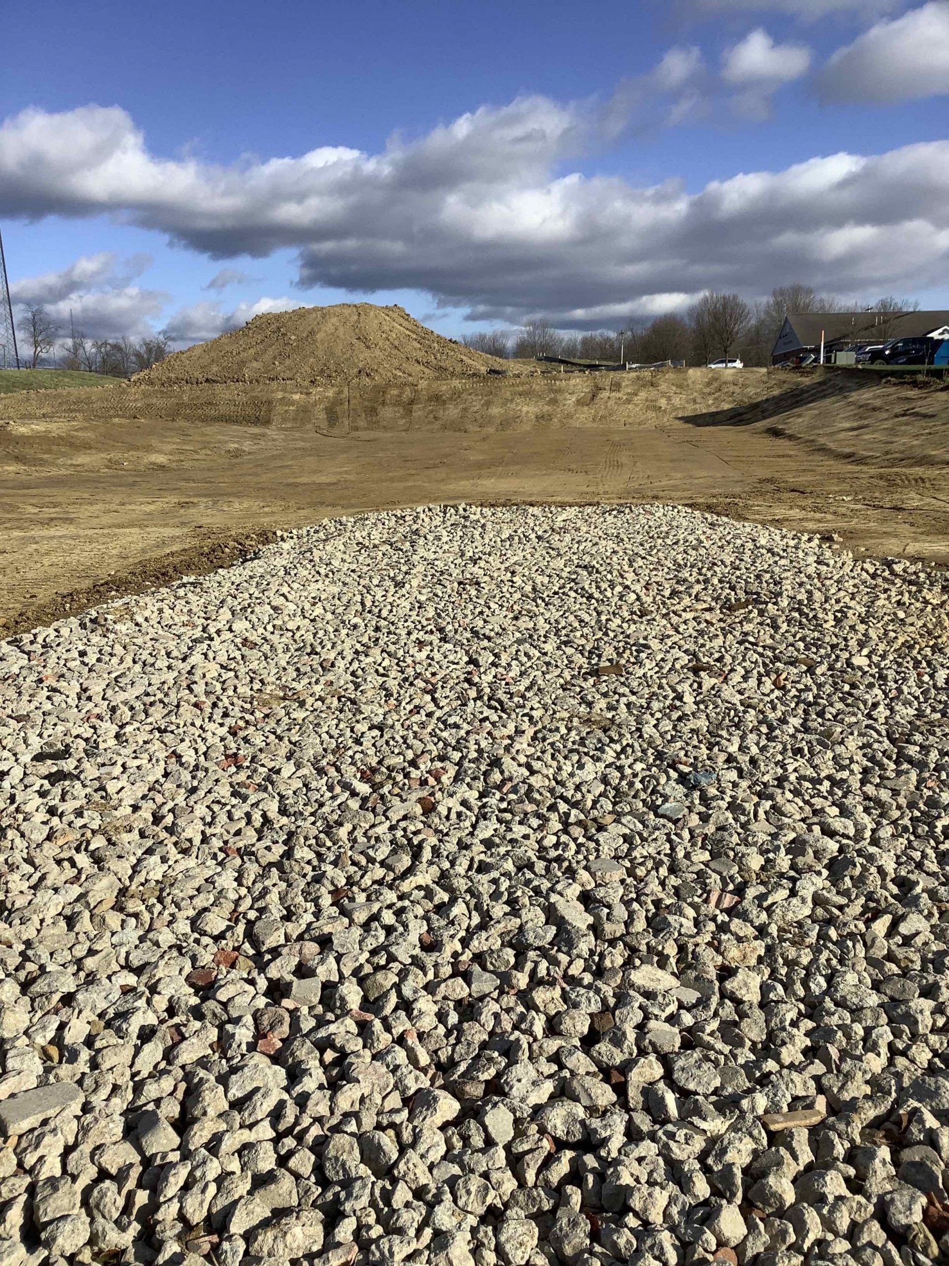 Pile of gray gravel in the foreground, dirt hill in the background, blue sky with clouds.