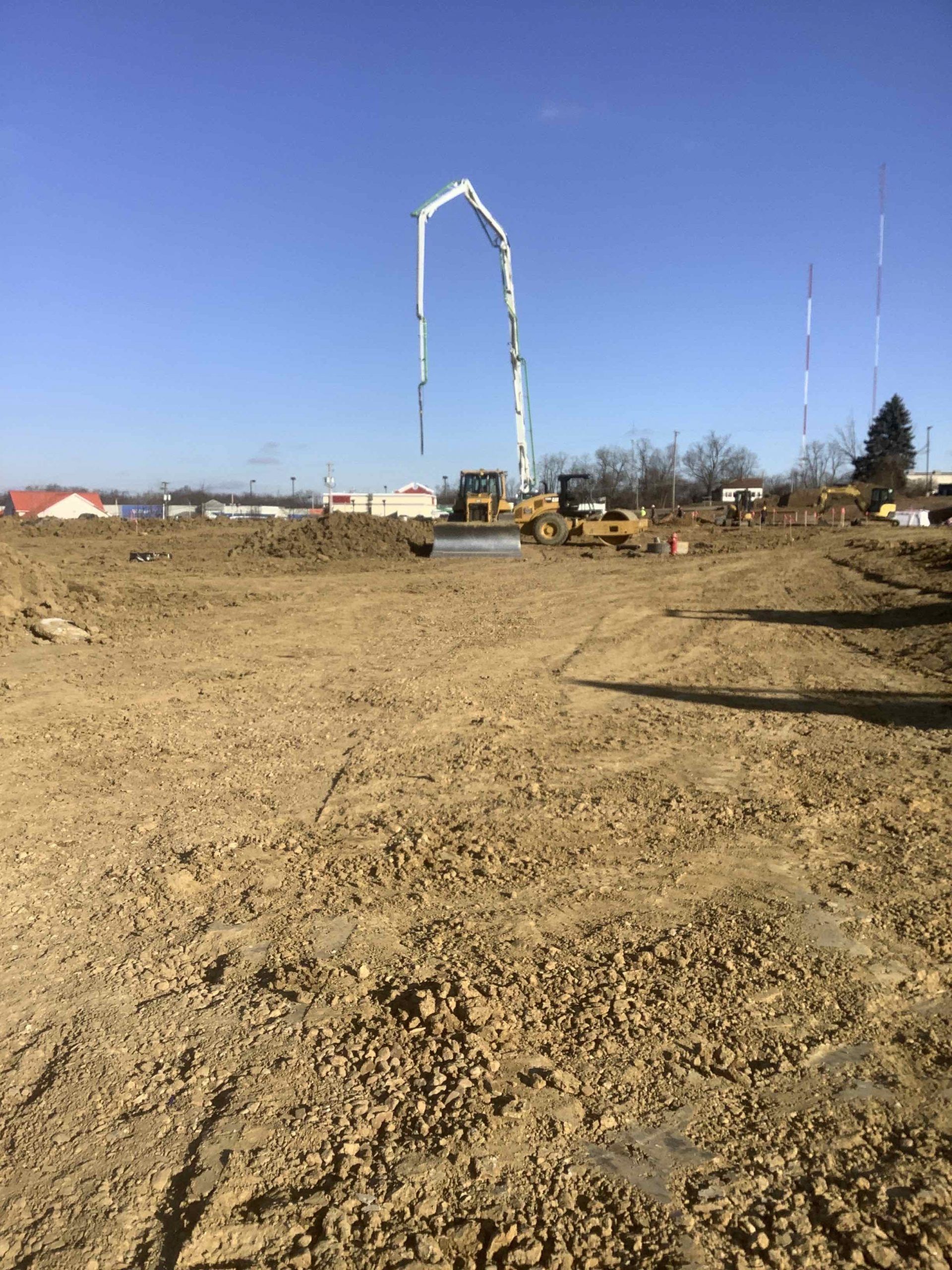 Construction site with concrete pump, bulldozer, and dirt. Blue sky overhead.