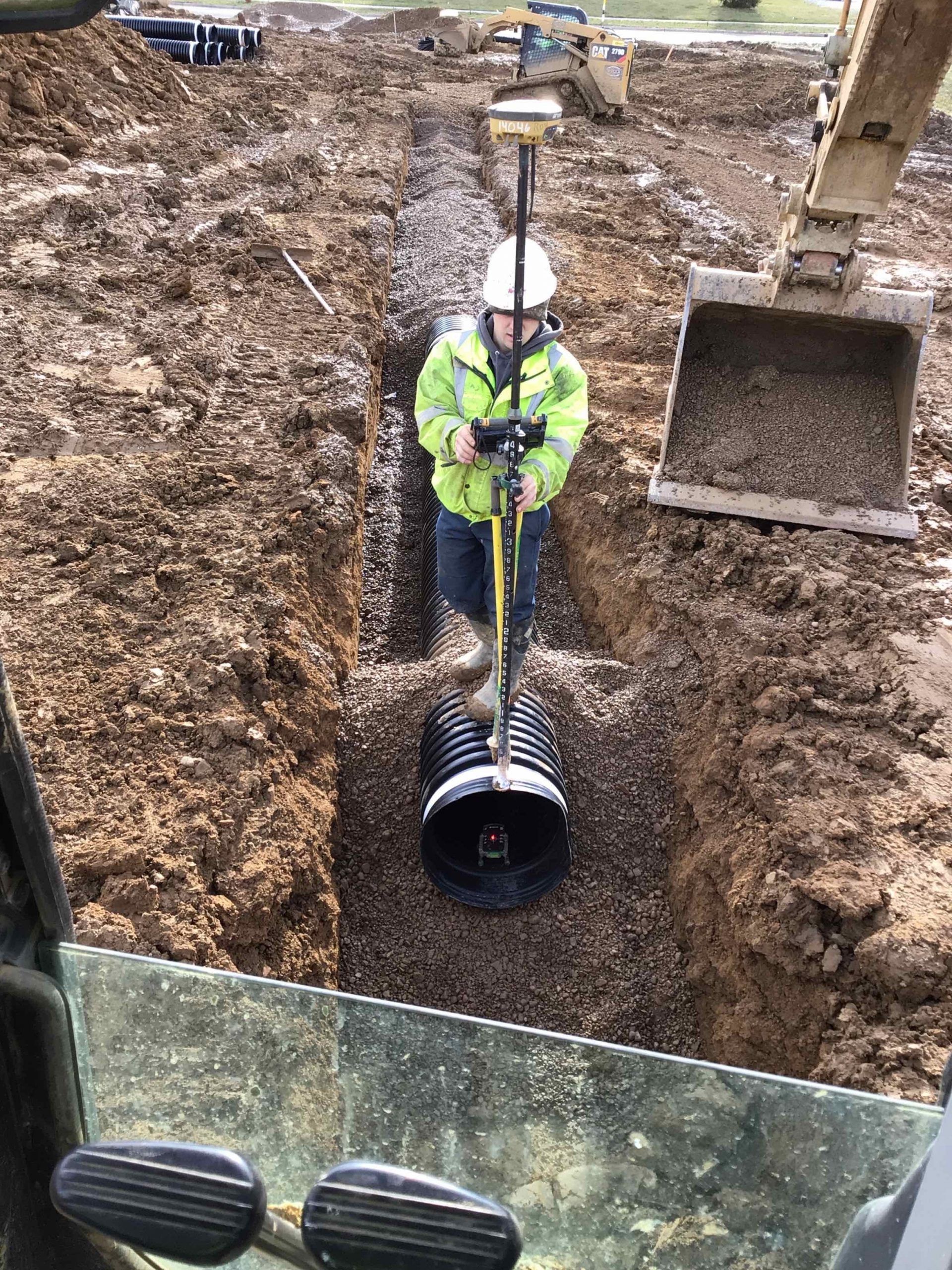 Shrock Excavating team compacting soil for drainage pipe installation. Expert utility trenching and site work.
