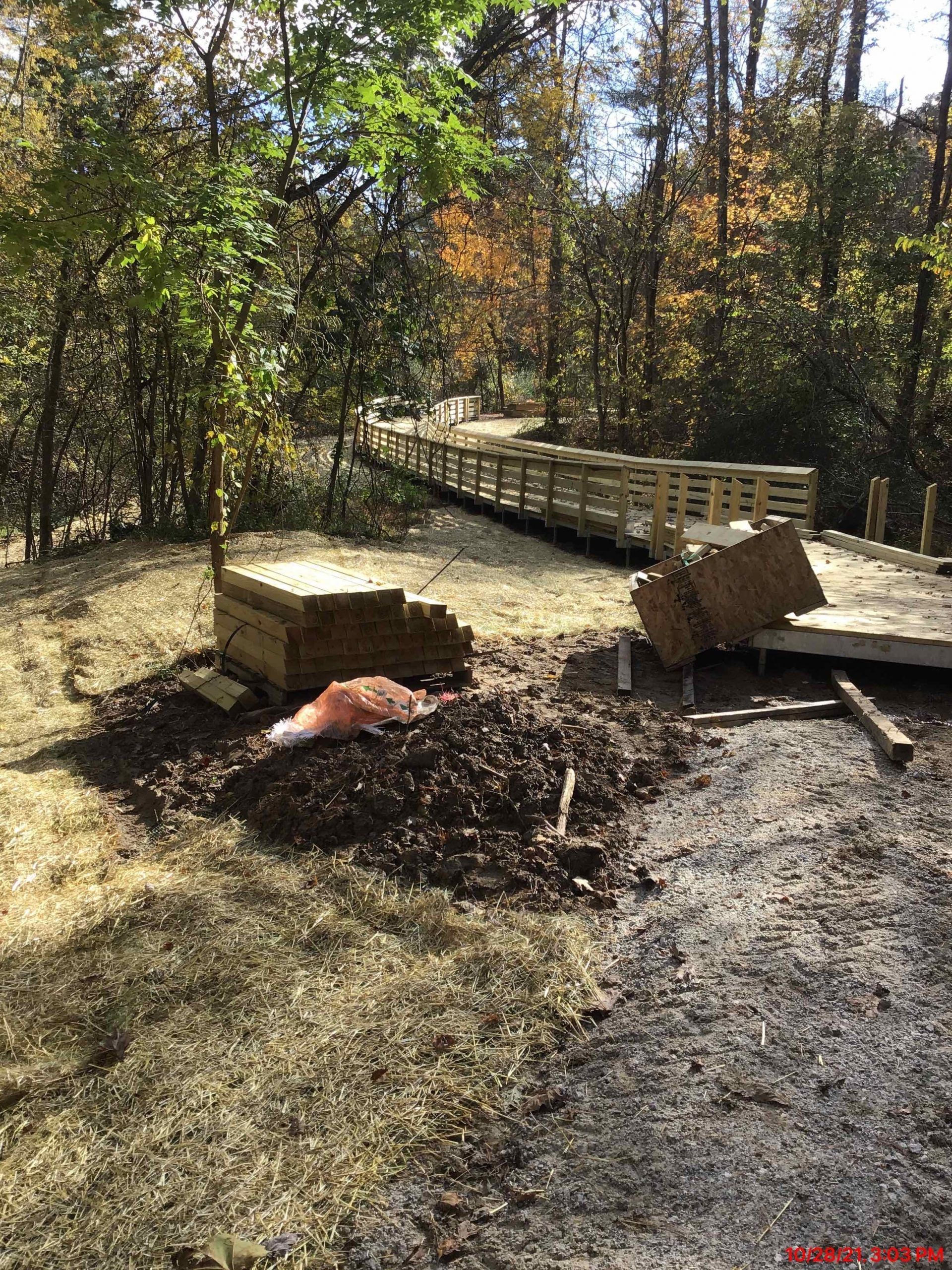 Wood walkway under construction in a wooded area with piles of materials nearby.