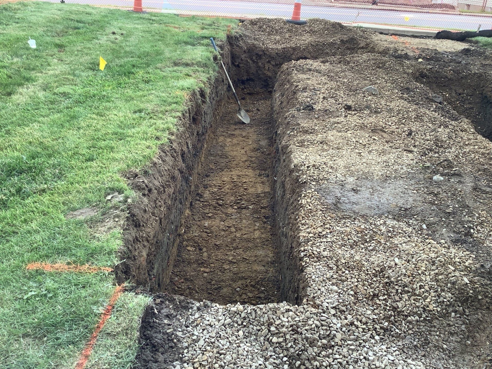 A rectangular trench is dug into a lawn; the edges are lined with dark clumps, soil, and gravel.
