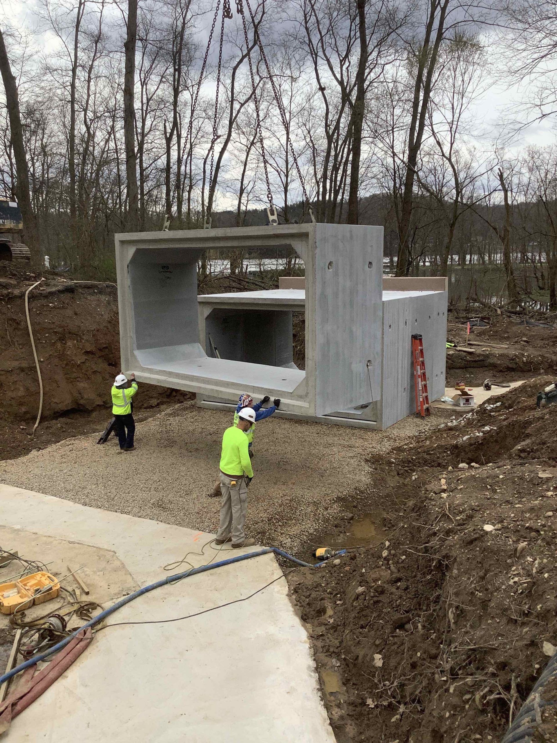 Construction workers near a large concrete culvert being installed in an outdoor setting.