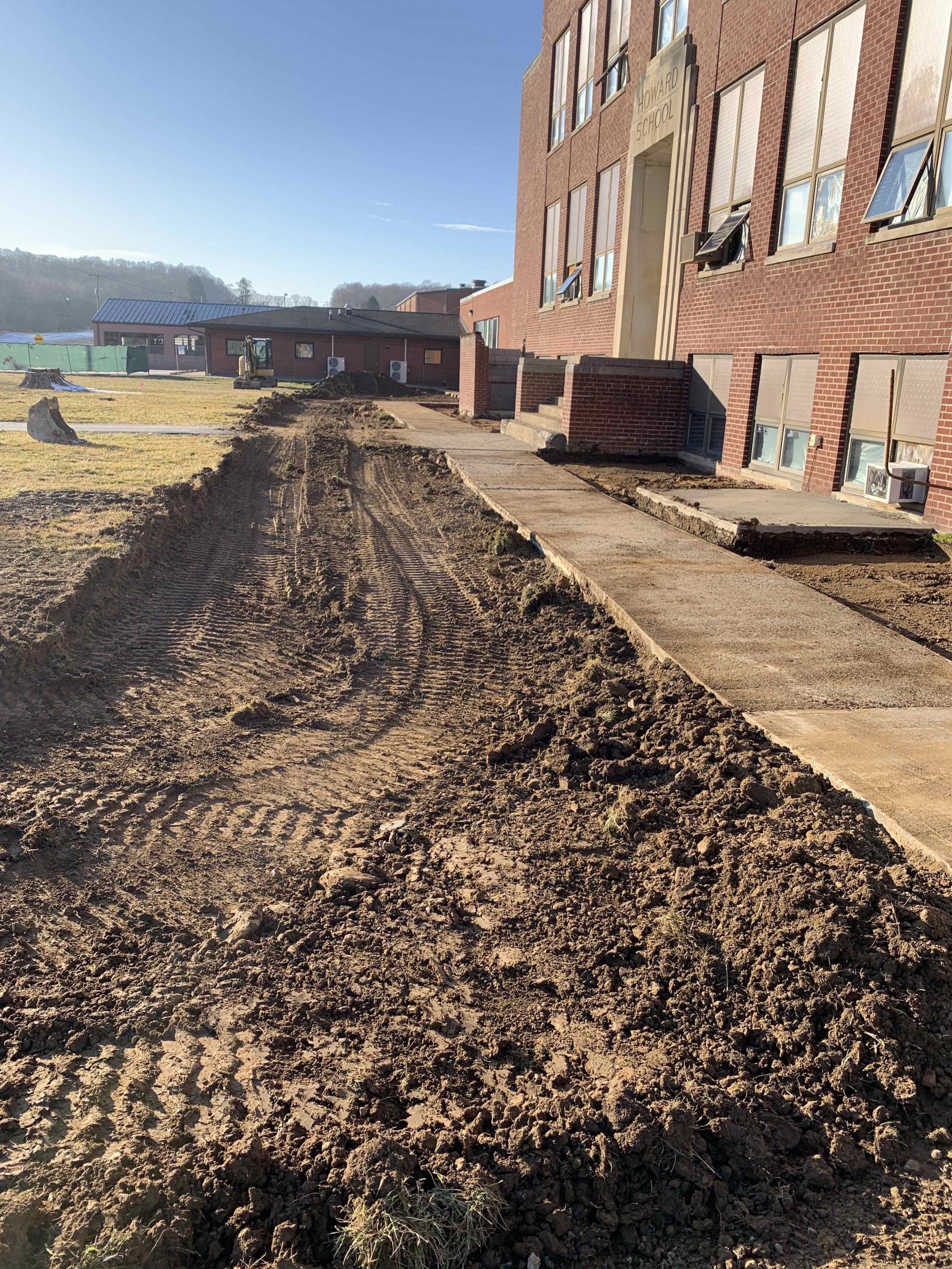 Construction site: Dirt path alongside a brick building with boarded windows. Brown earth and sky.