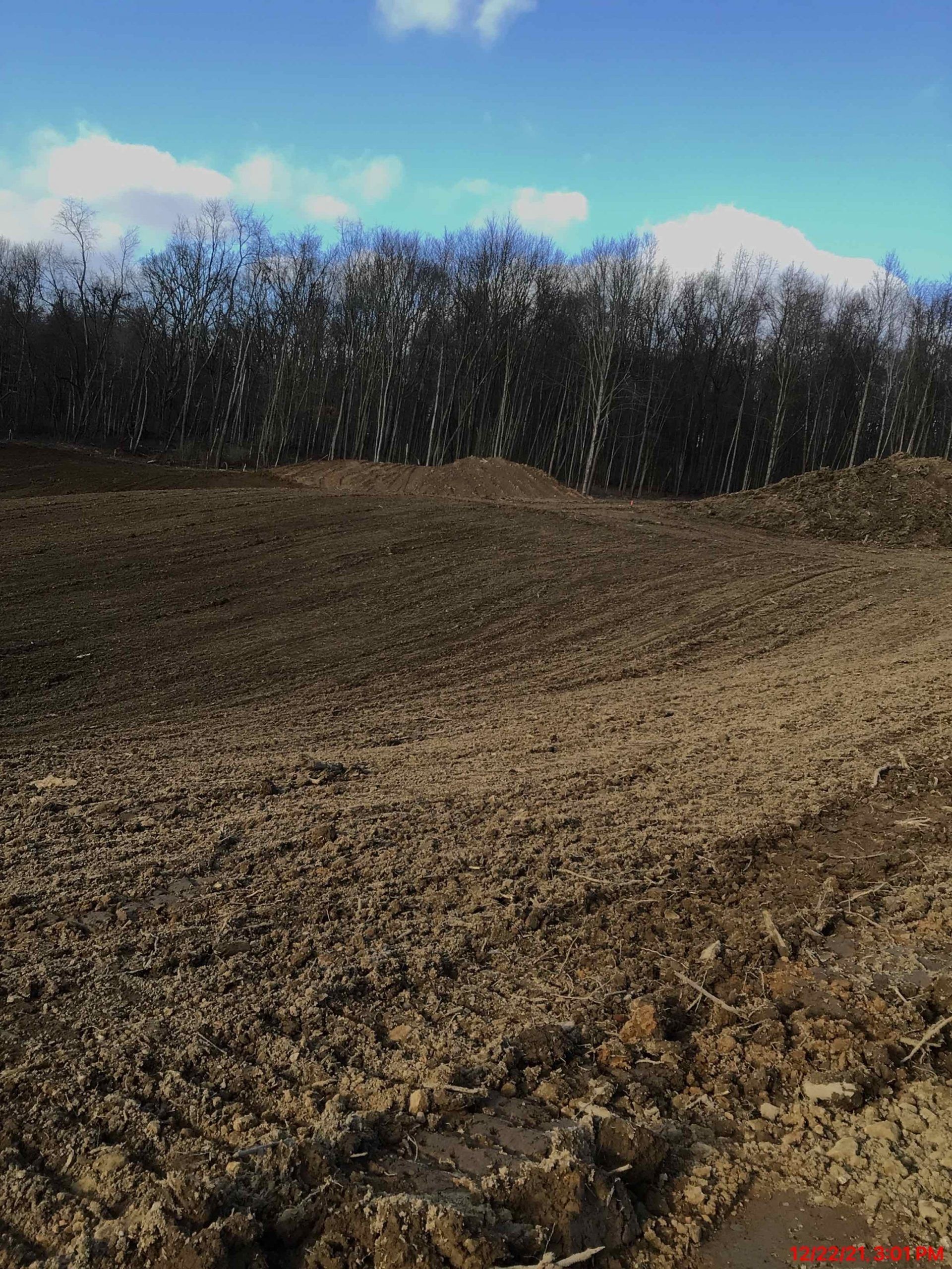 A muddy brown field with a treeline under a blue sky with some clouds.