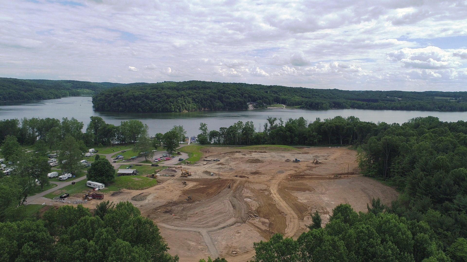 A construction site near a lake, surrounded by trees under a cloudy sky.
