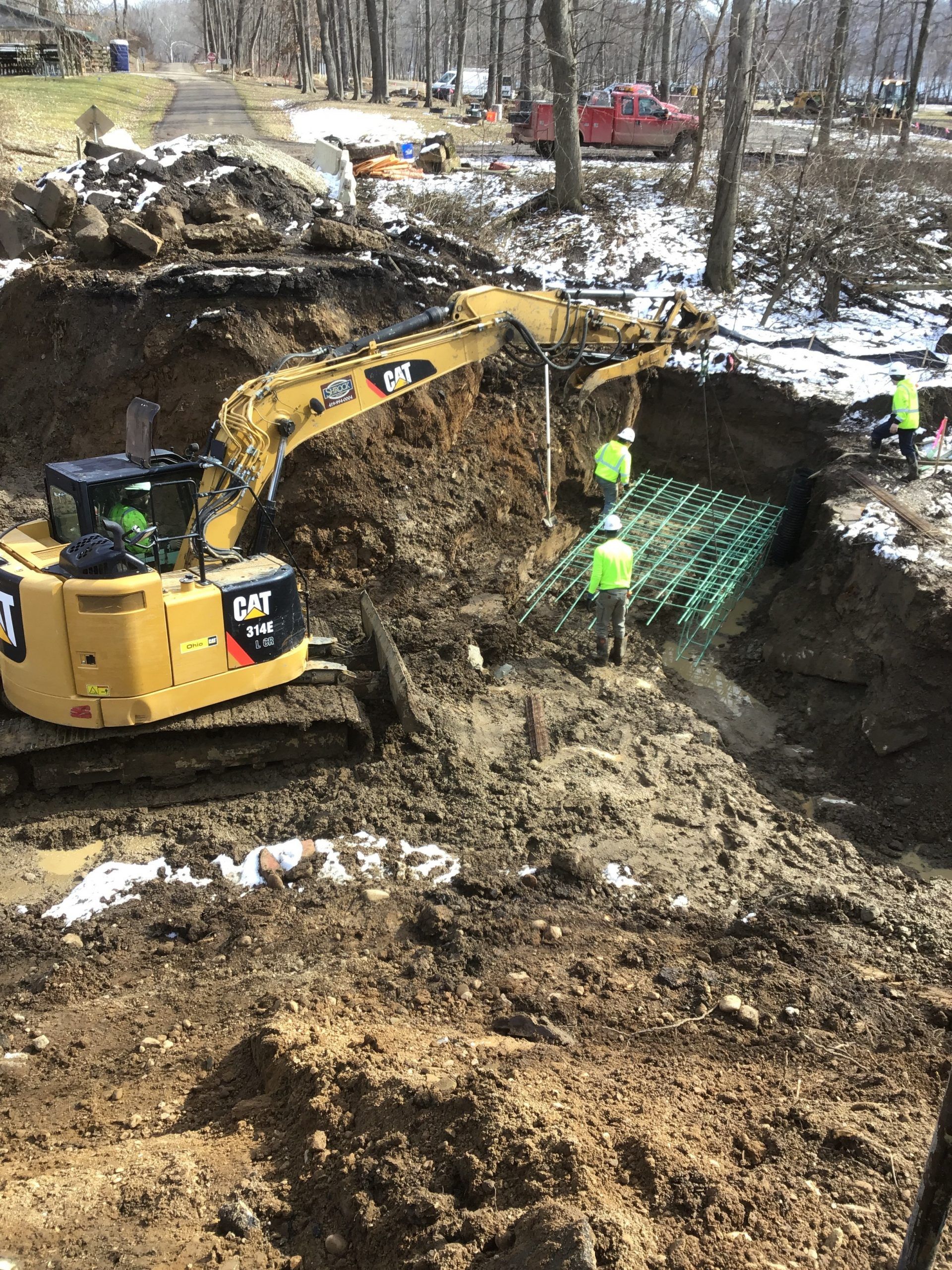 Yellow excavator at work in a muddy construction site with workers in safety vests.