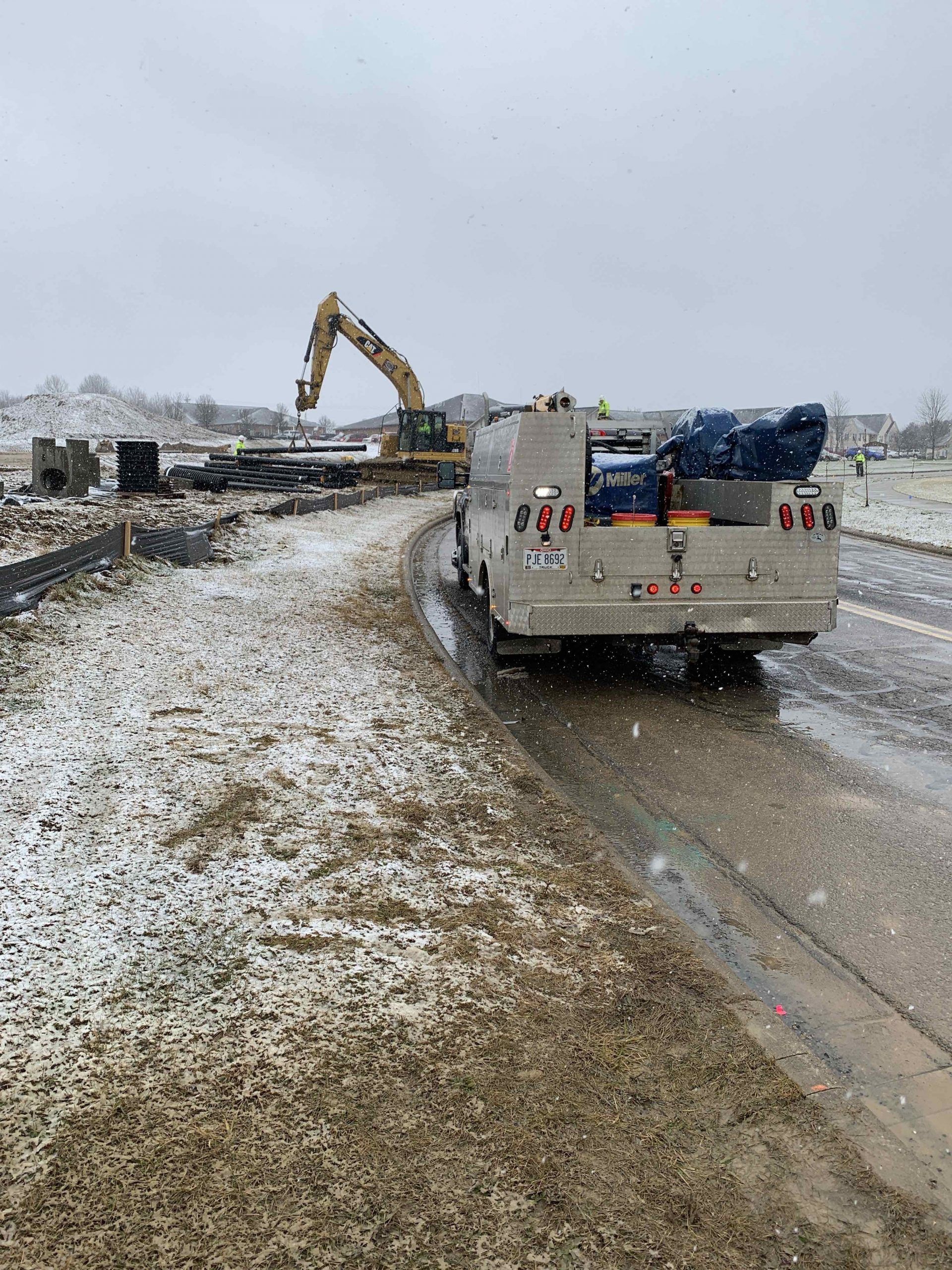 Work truck on muddy construction site with excavator in the snowy background.