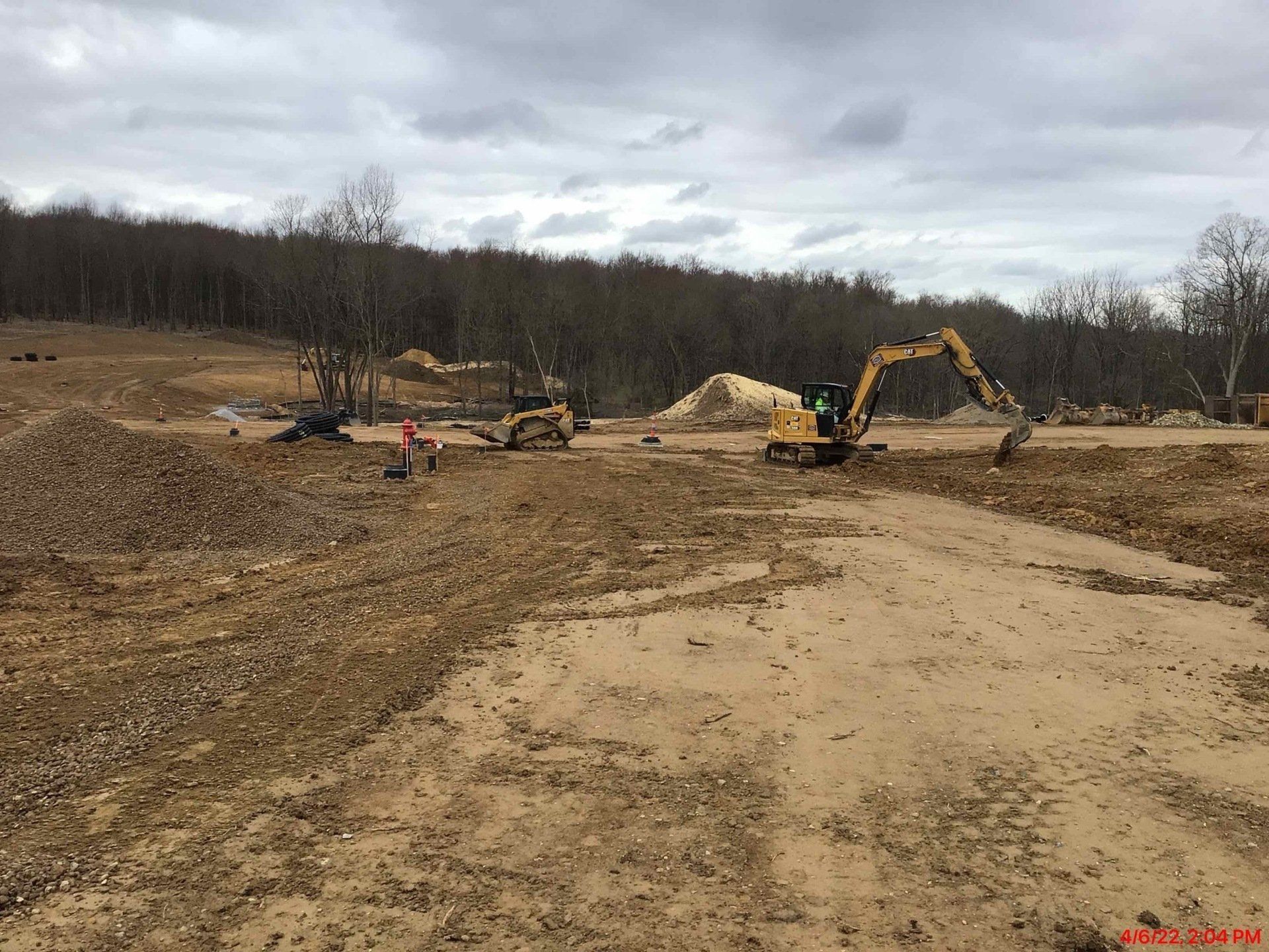 Construction site with heavy machinery, clearing land near a forest under a cloudy sky.