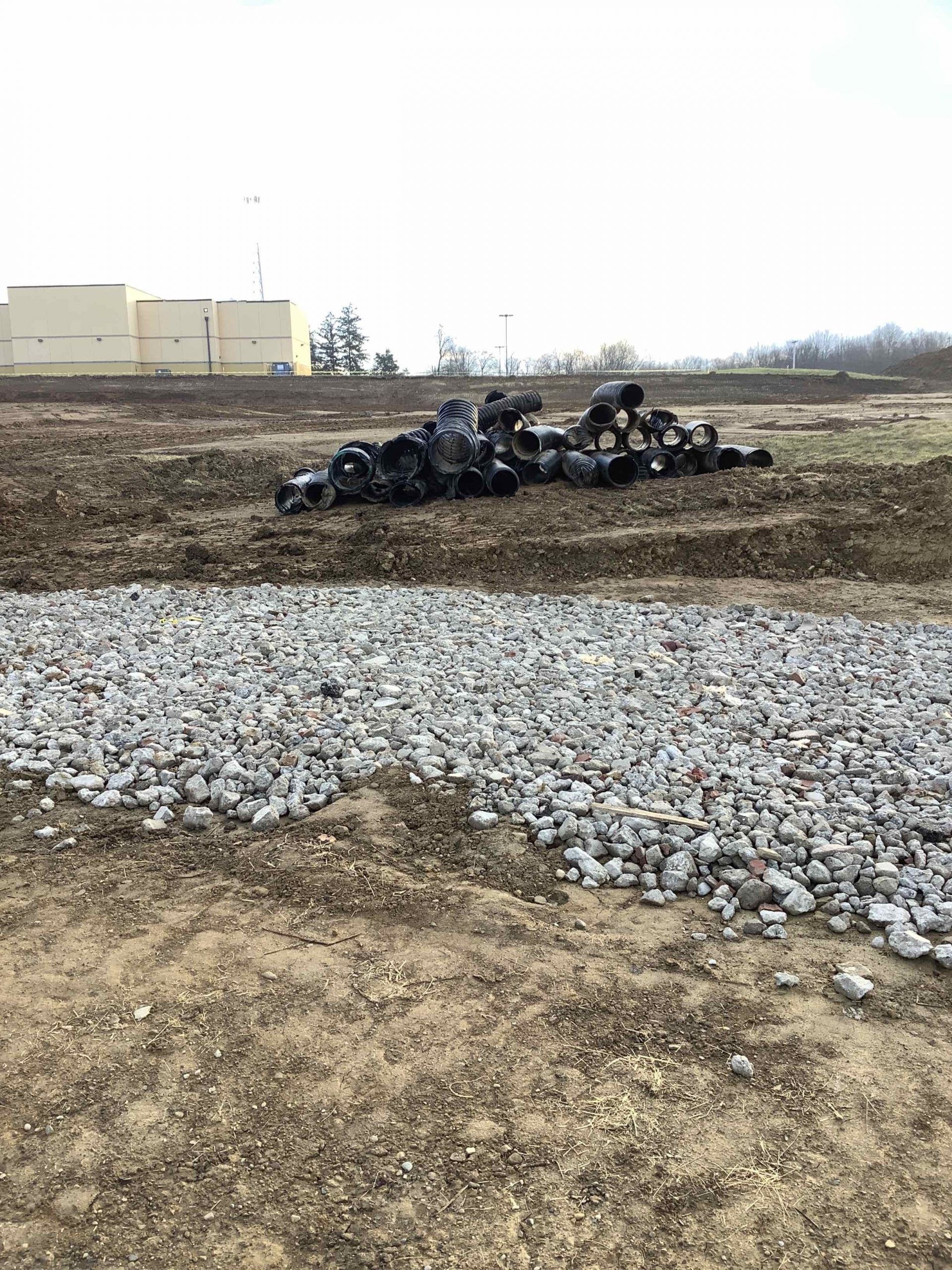 Pile of tires and gravel on a construction site with tan buildings in the background.