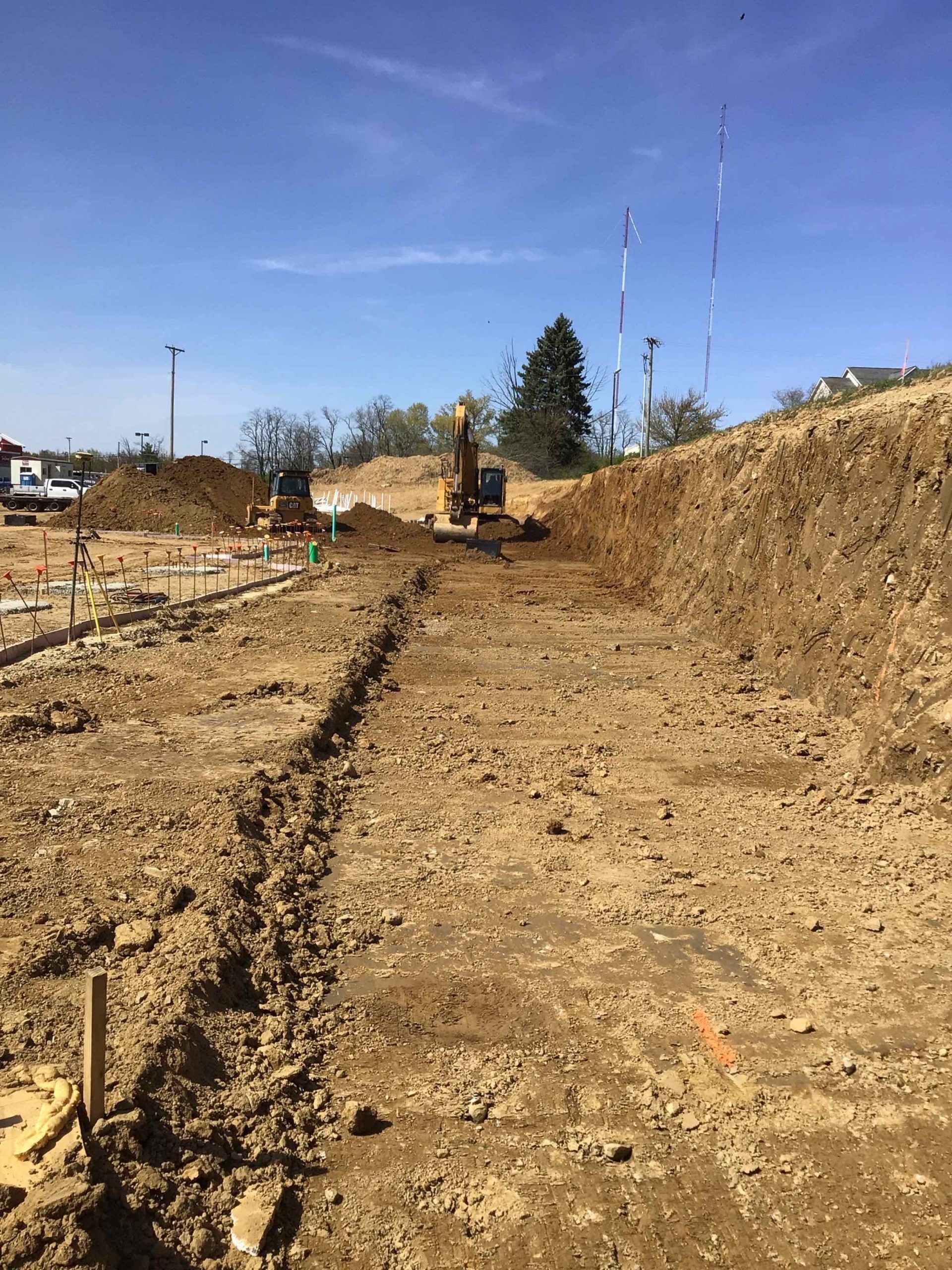 Construction site with an excavator digging a trench in dirt under a blue sky.