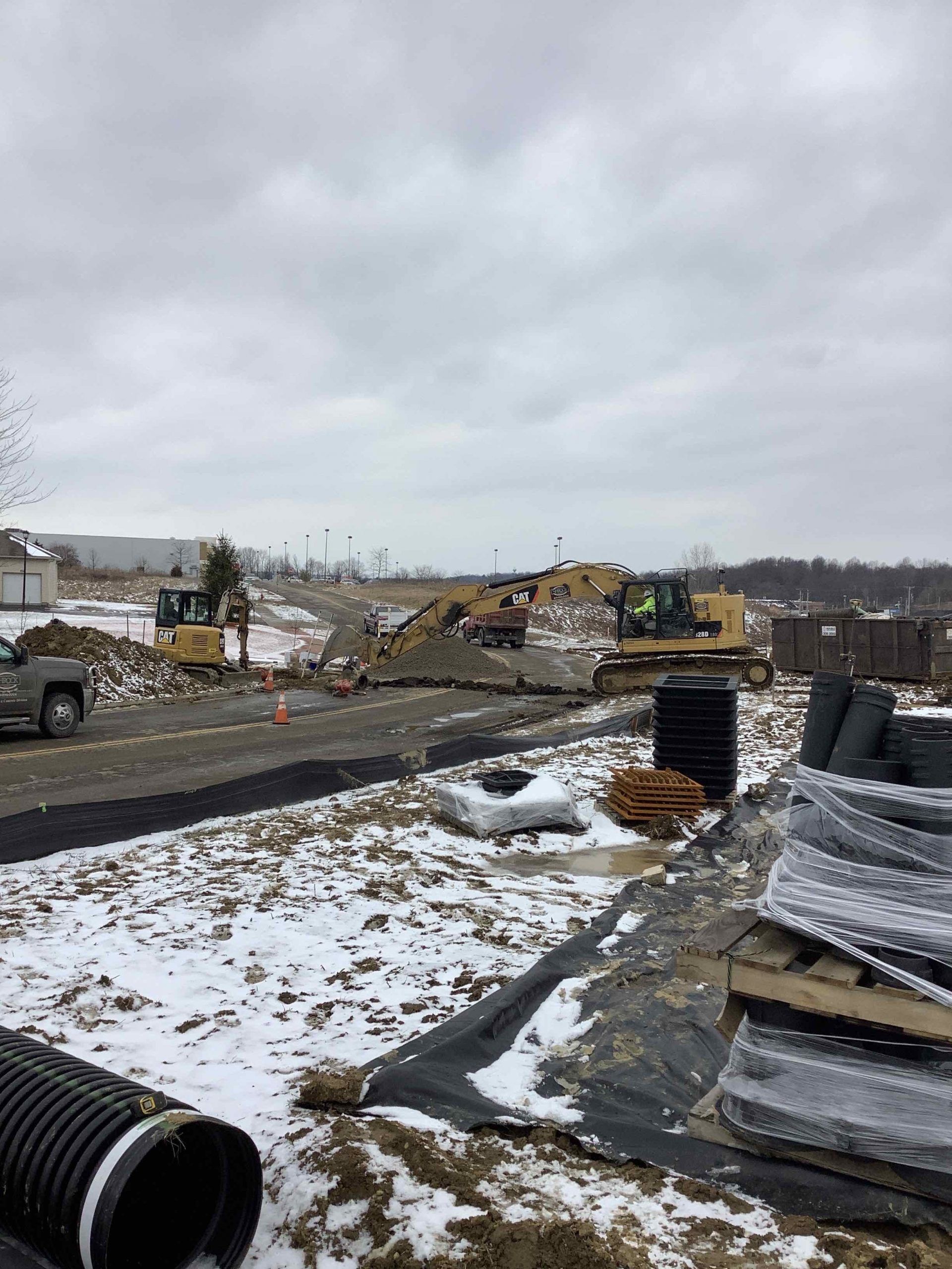 Construction site with heavy machinery, piles of dirt, and snow under cloudy sky.