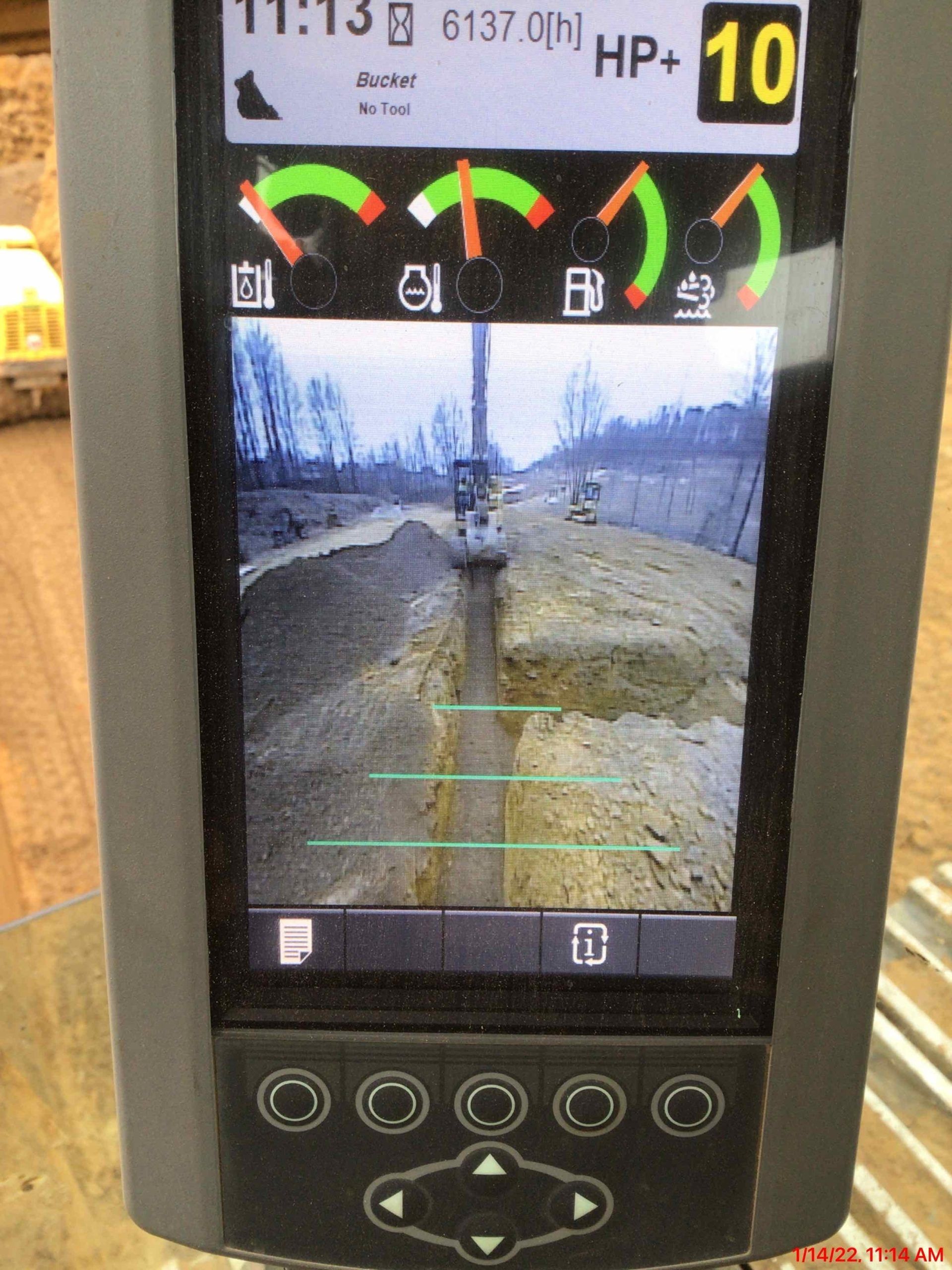 Screen showing a camera view of a trench with green leveling lines, and gauges for battery, oil, fuel and engine temperature.