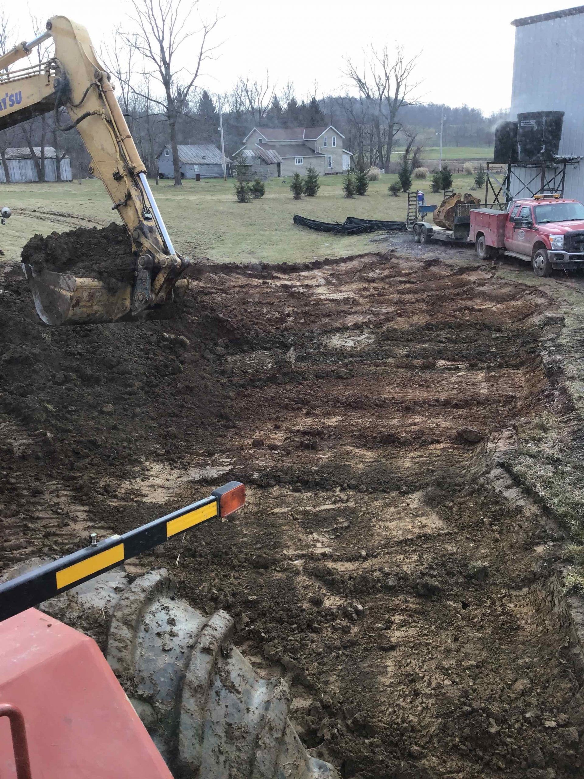 An excavator scoops up dirt in a field; a fire truck is parked nearby.