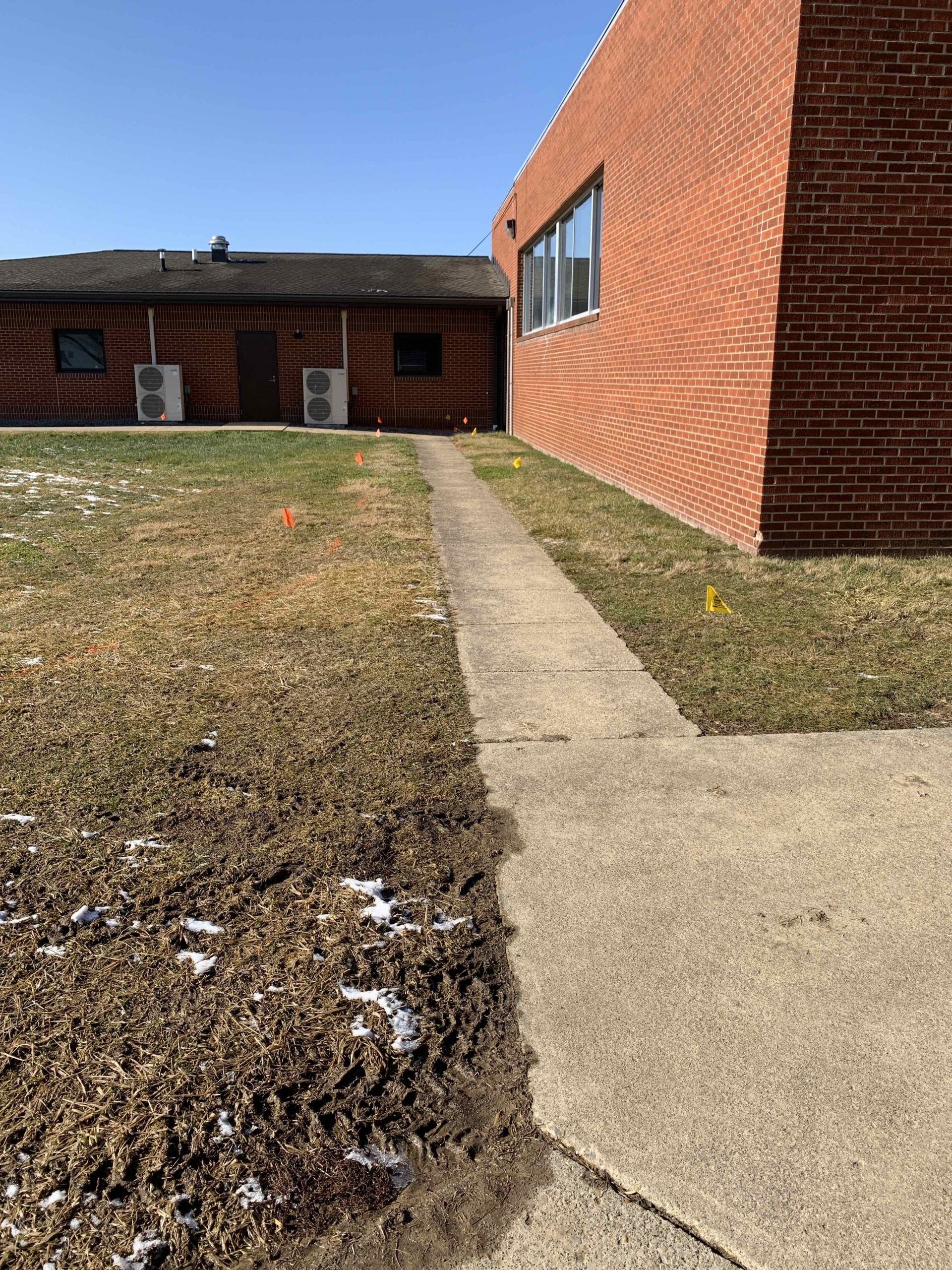 Pathway between brick buildings and patches of snow on grass.