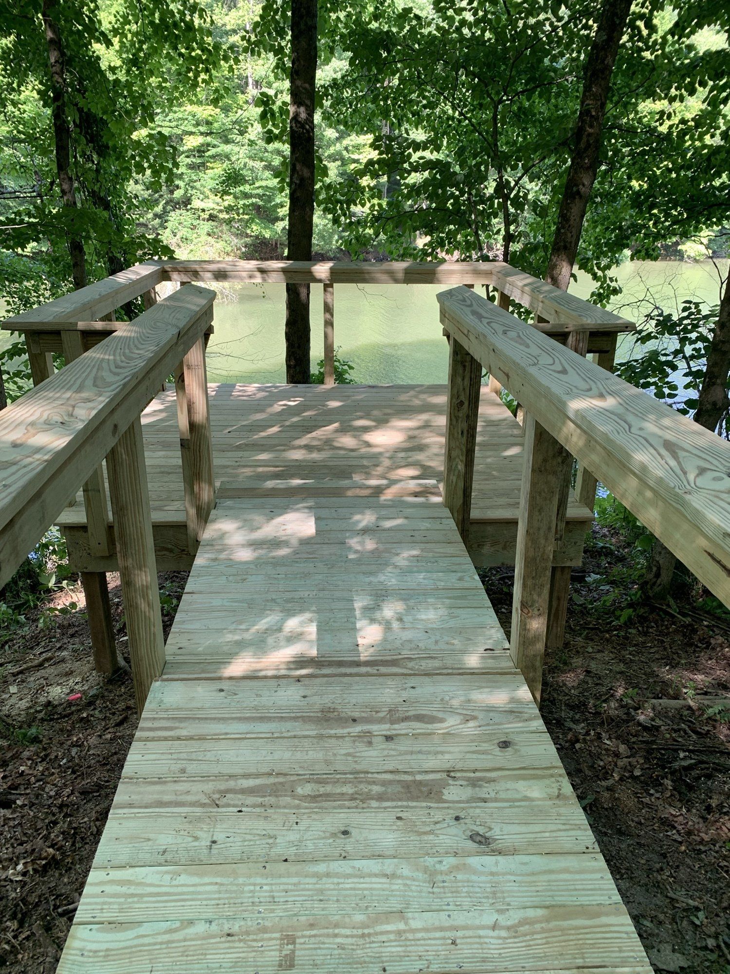 Wooden boardwalk leading to a lake overlook in a shaded forest.