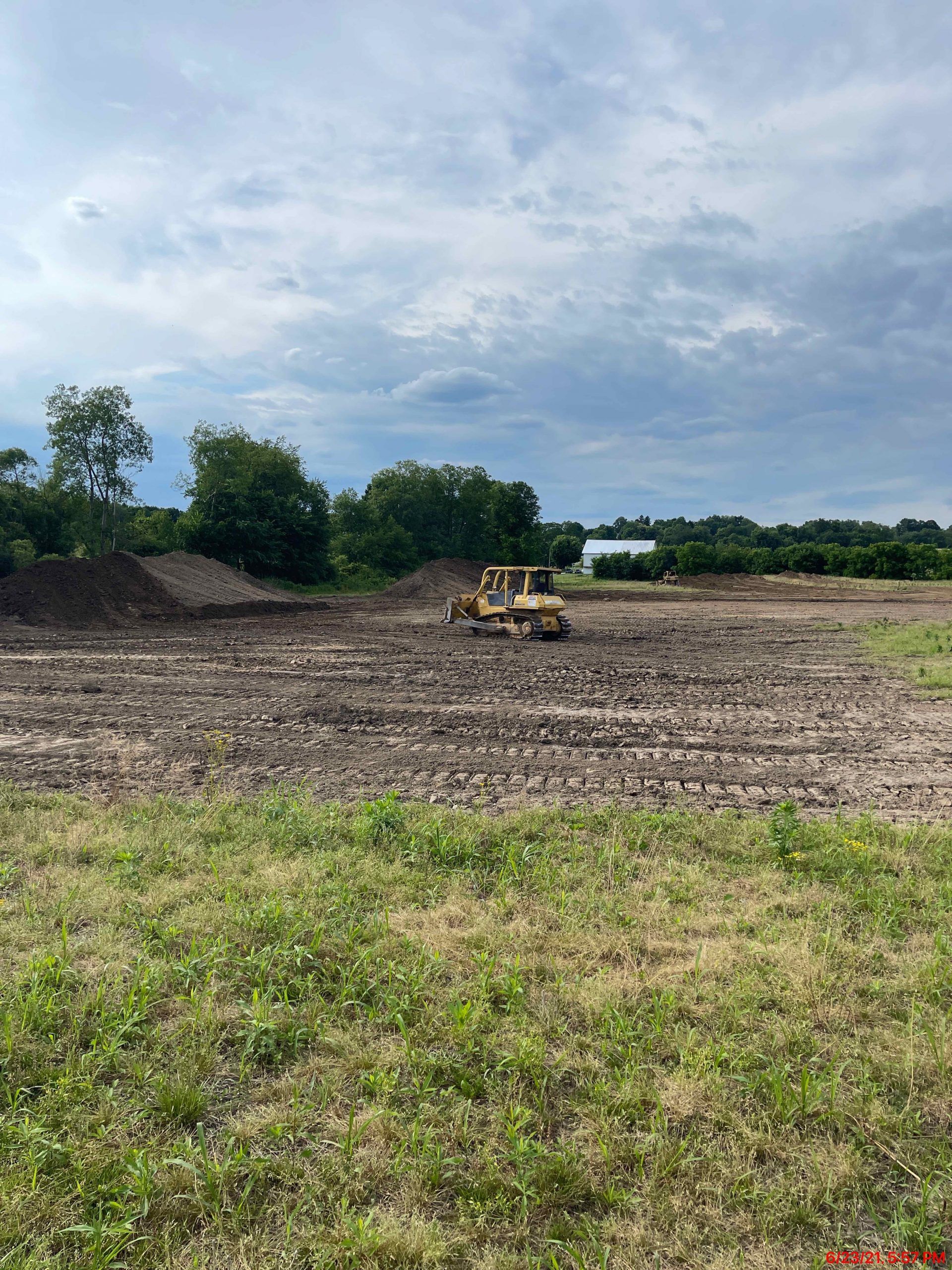 A bulldozer working on a muddy field under a cloudy sky, with trees in the background.