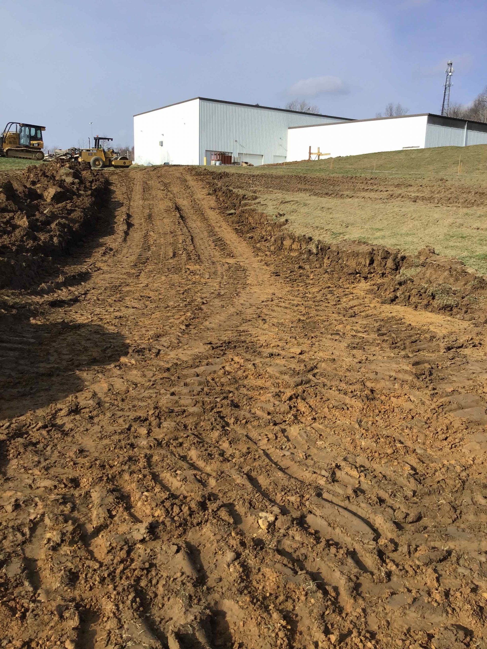 Muddy dirt path leading uphill toward a white building; construction equipment visible.