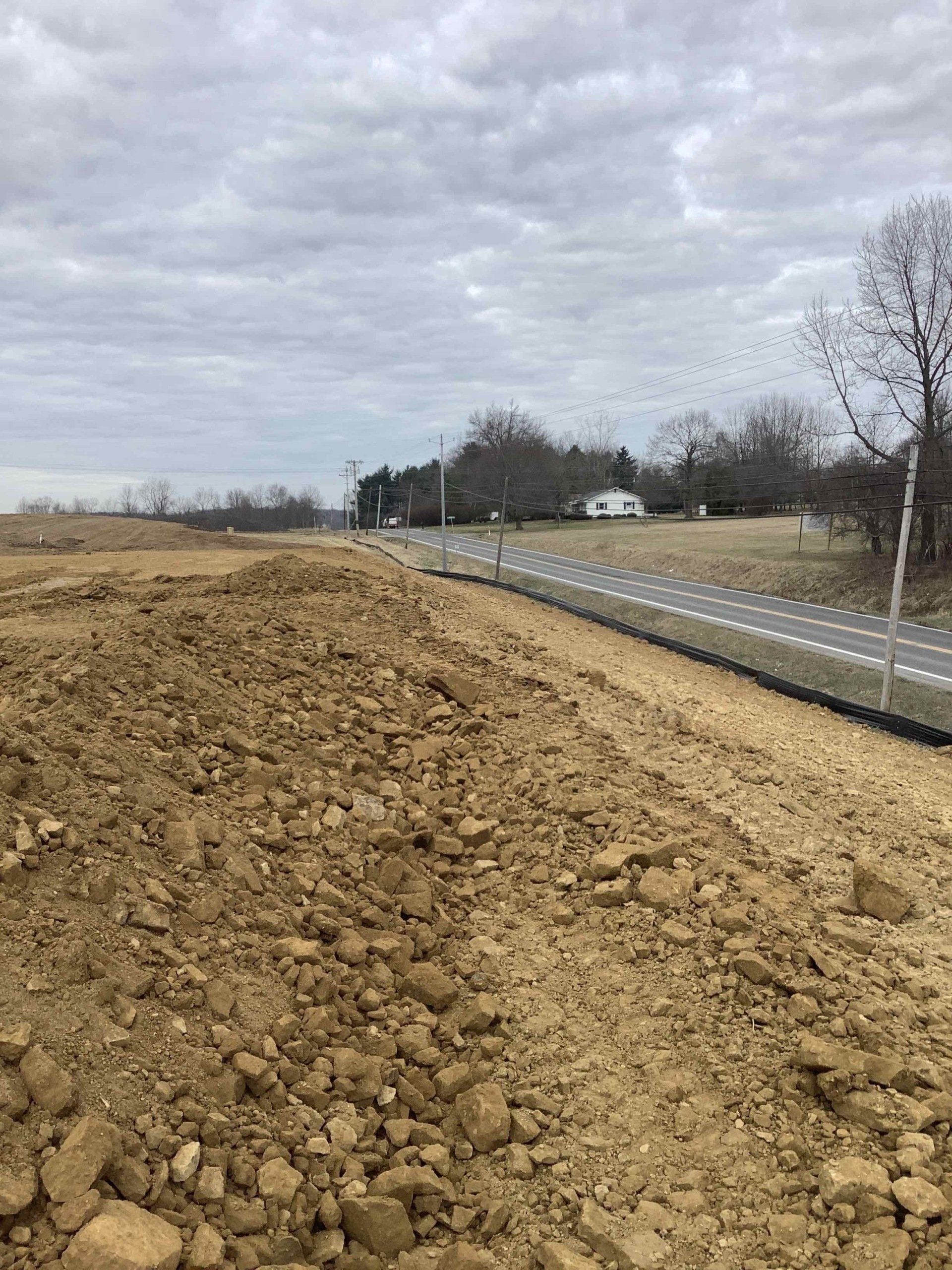 Dirt pile alongside a freshly paved road under an overcast sky.