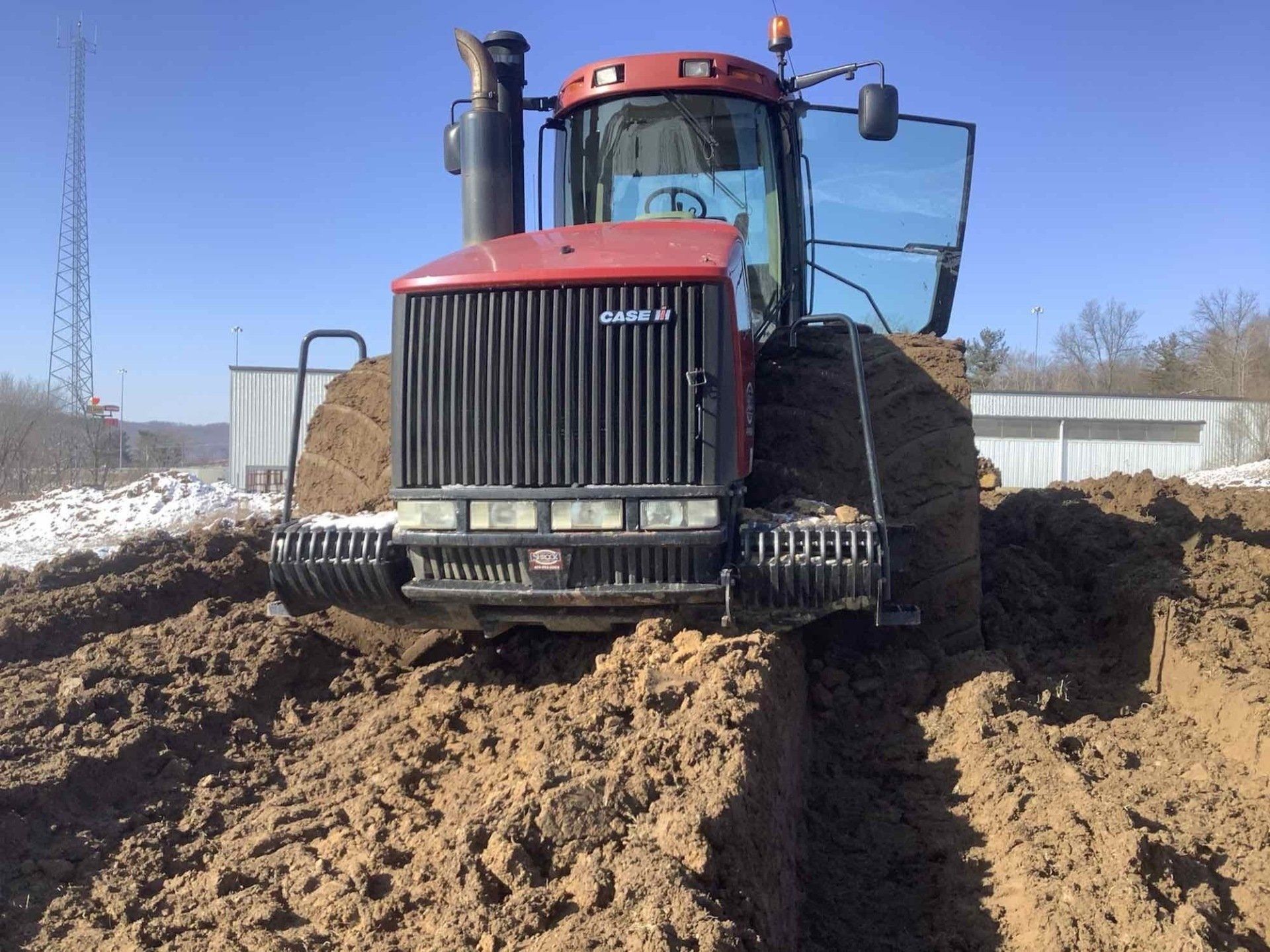 Red tractor plowing through a pile of brown earth on a sunny day.