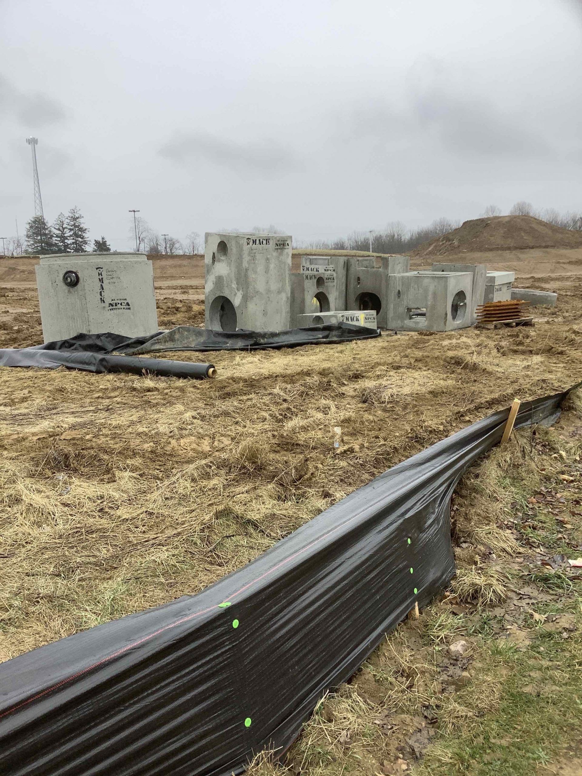 Concrete structures sit on a field, black fabric in foreground, overcast sky.