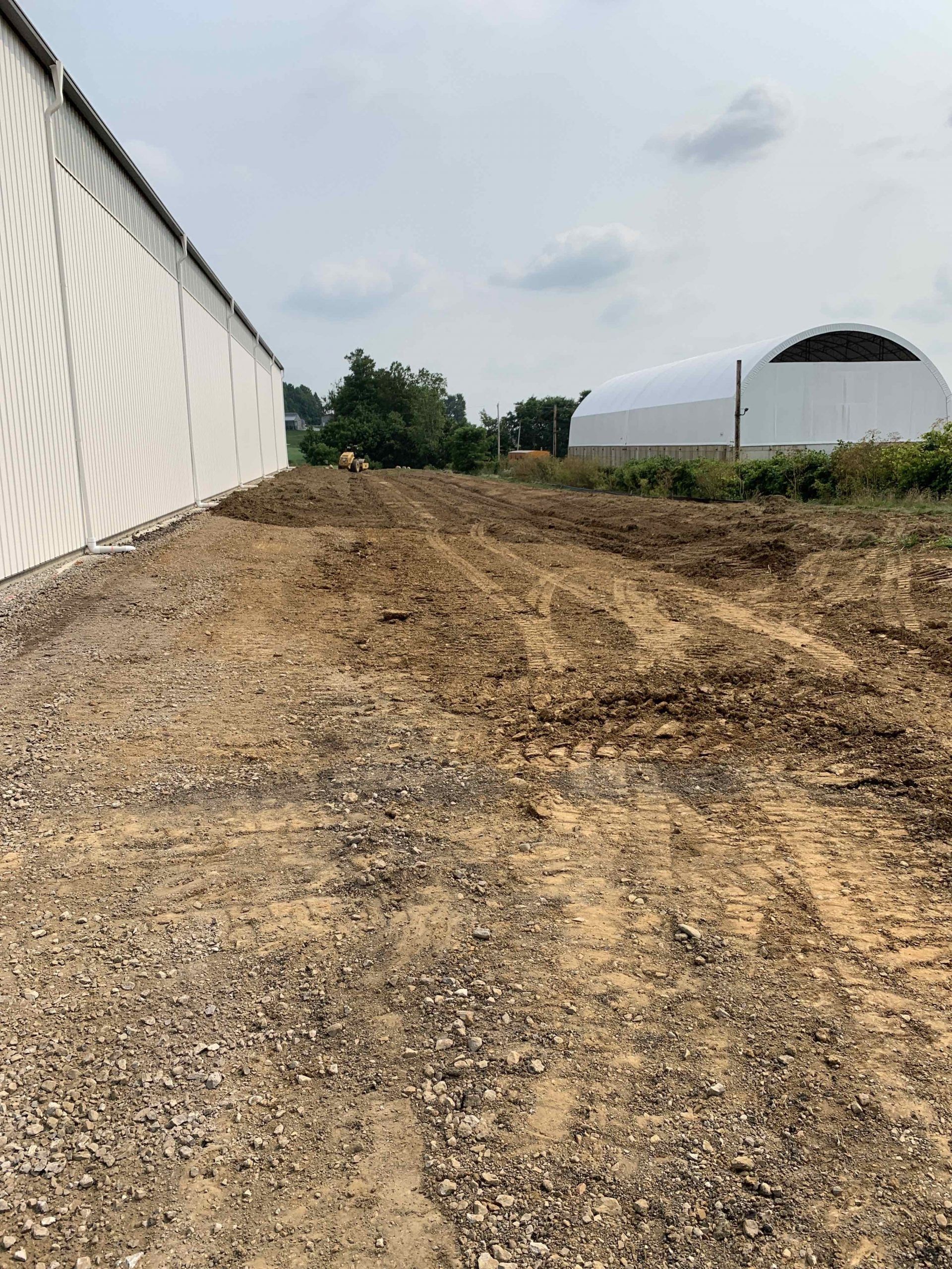 Dirt lot next to white building, with a curved white structure in the background under a cloudy sky.