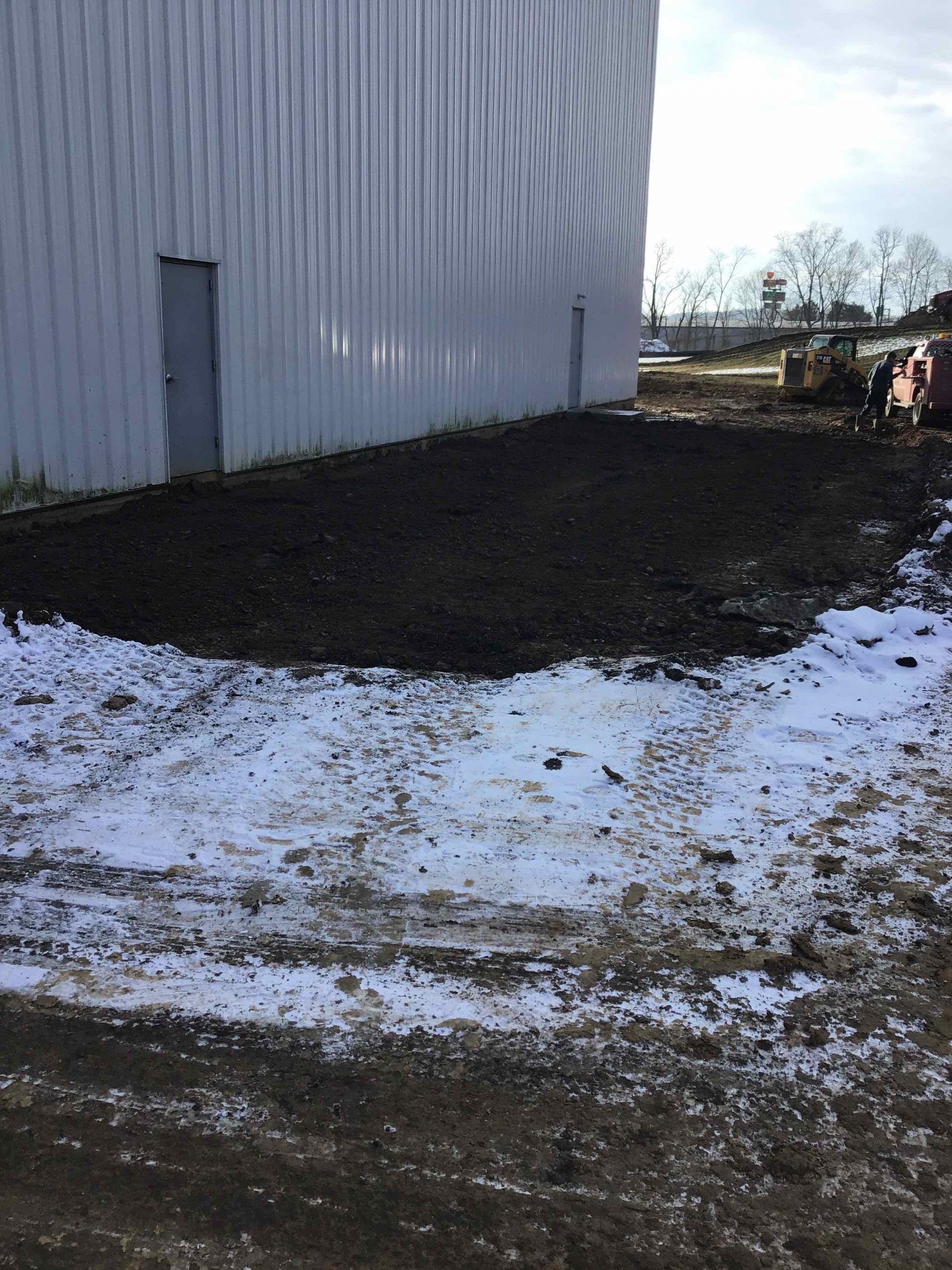 Exterior of a building with dark soil and patches of snow in front.