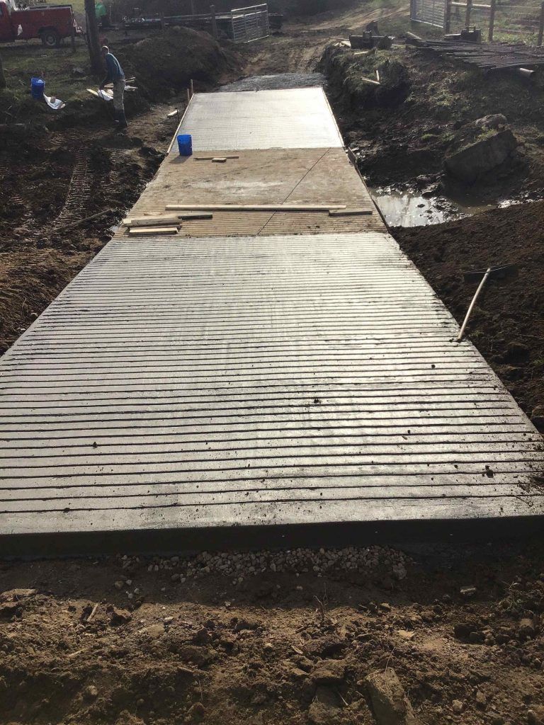 Newly poured concrete path with wood-grain texture in a dirt construction site.