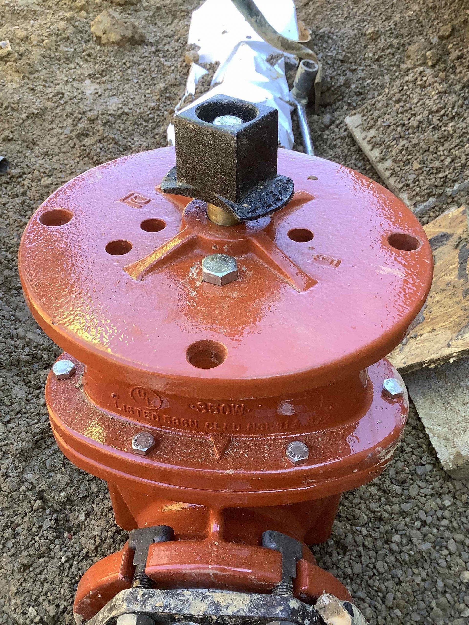 Orange water valve with square top, installed in the ground.