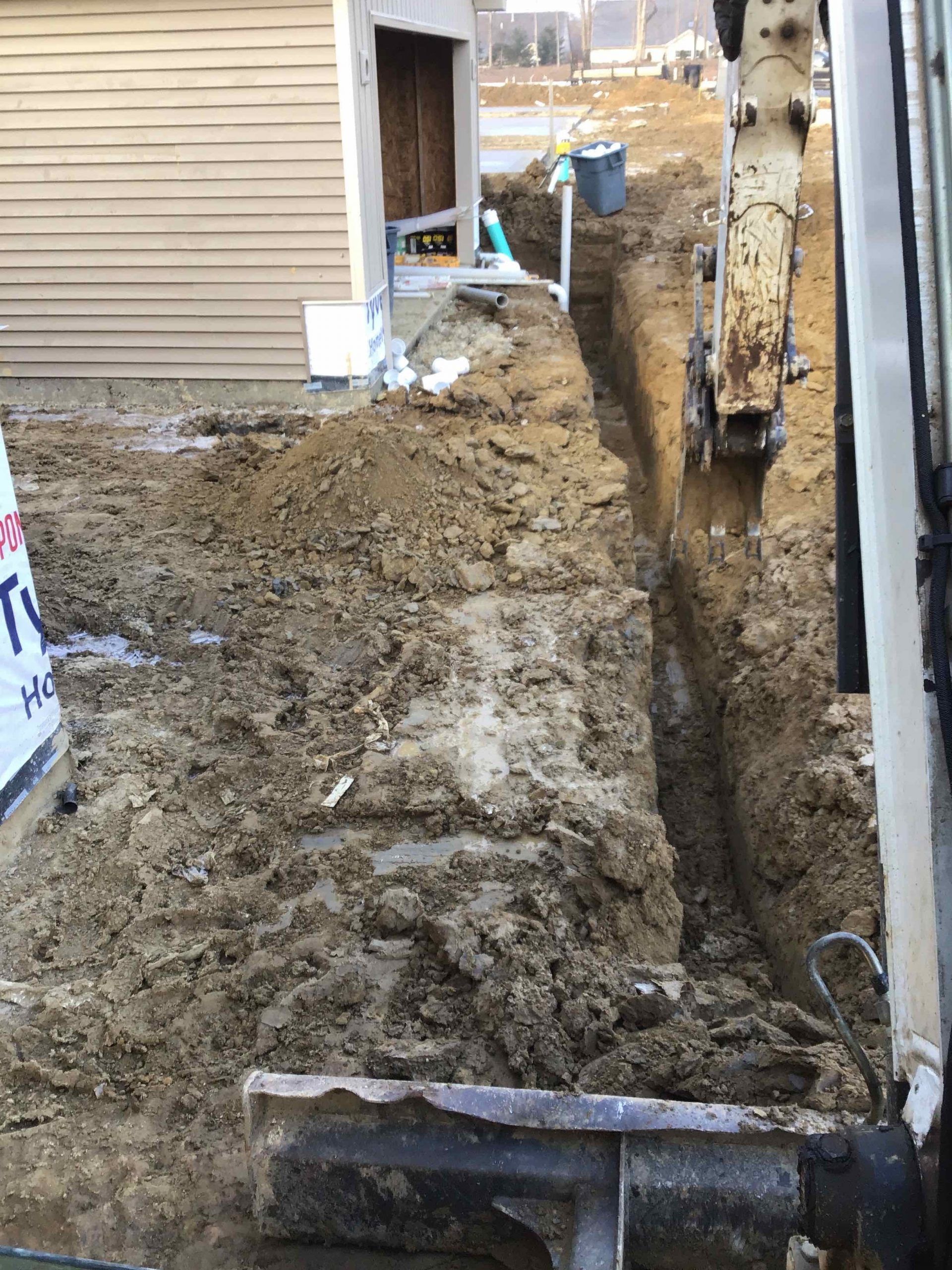 A backhoe digging a trench next to a building under construction.