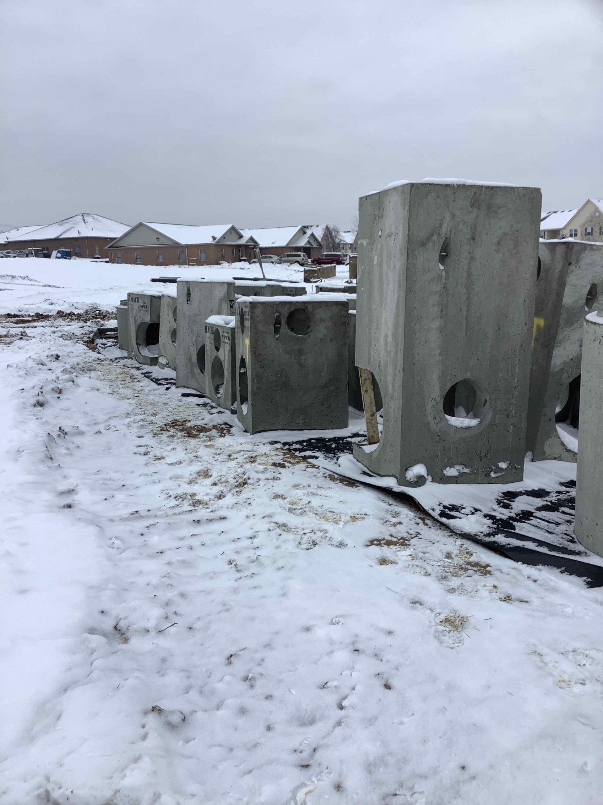 Concrete blocks on snow-covered ground; houses in the background under an overcast sky.