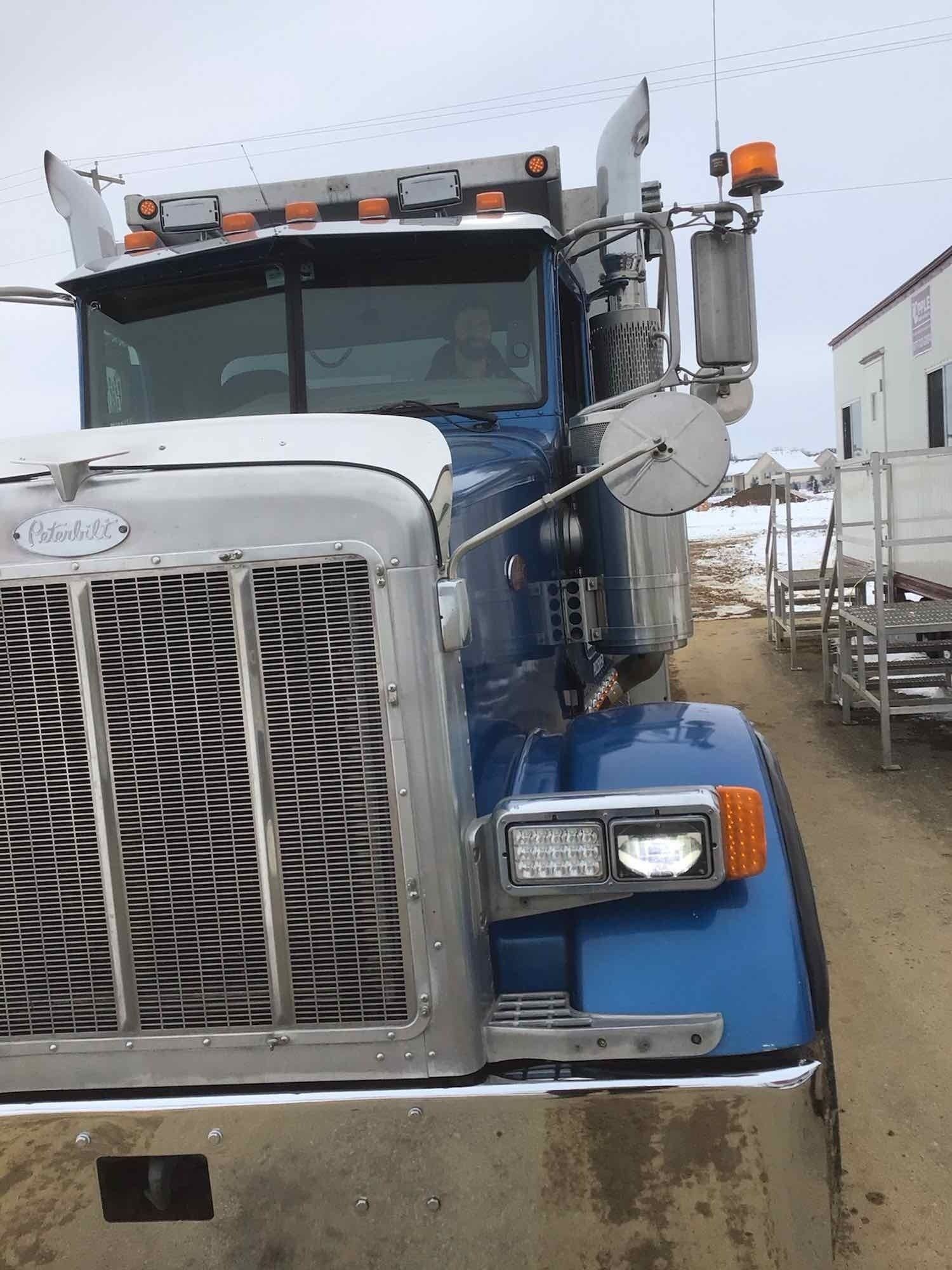 Blue and chrome Peterbilt semi-truck parked outdoors on a cloudy day.